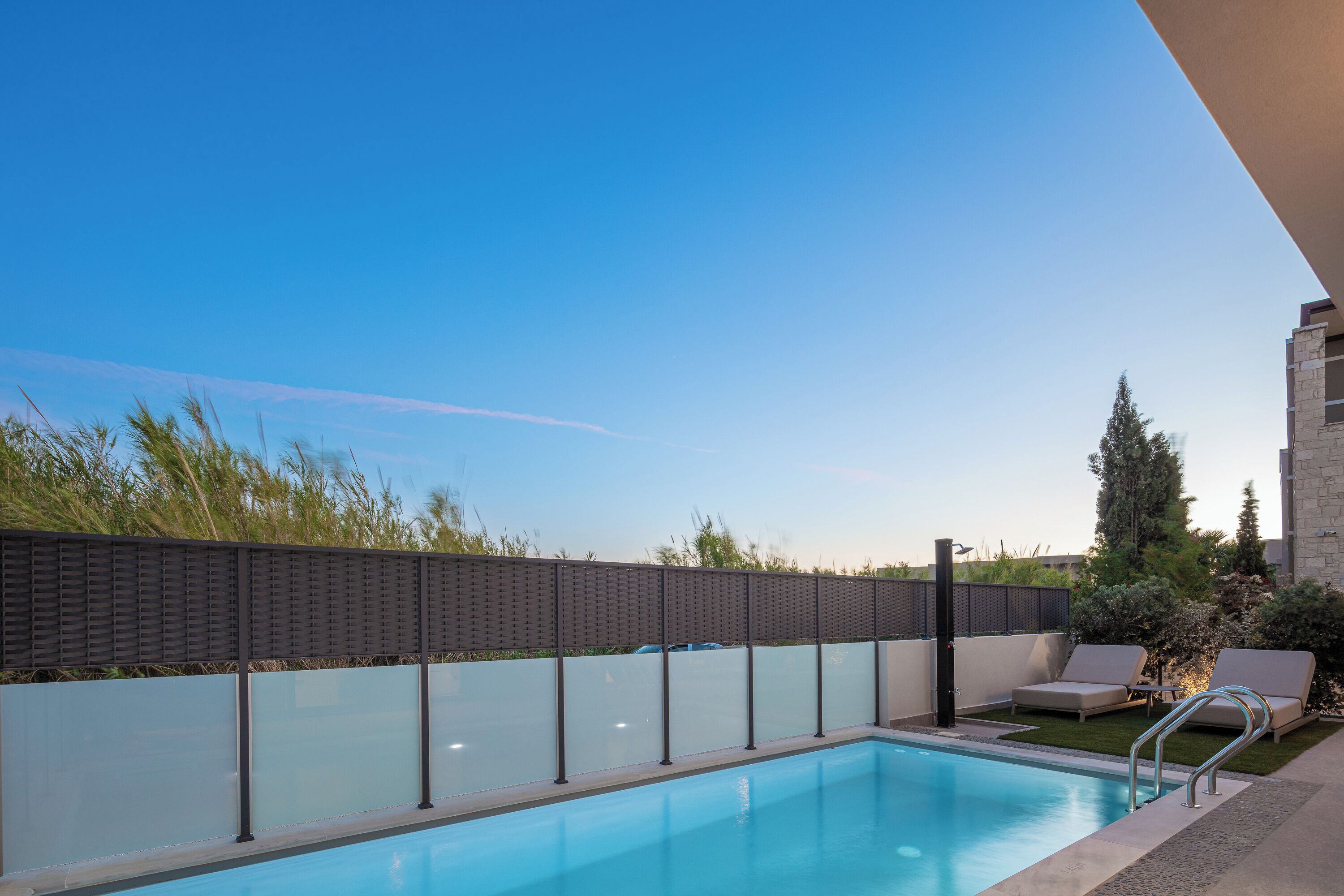 A swimming pool with a glass wall, lounge chairs, and a stone building in the background.