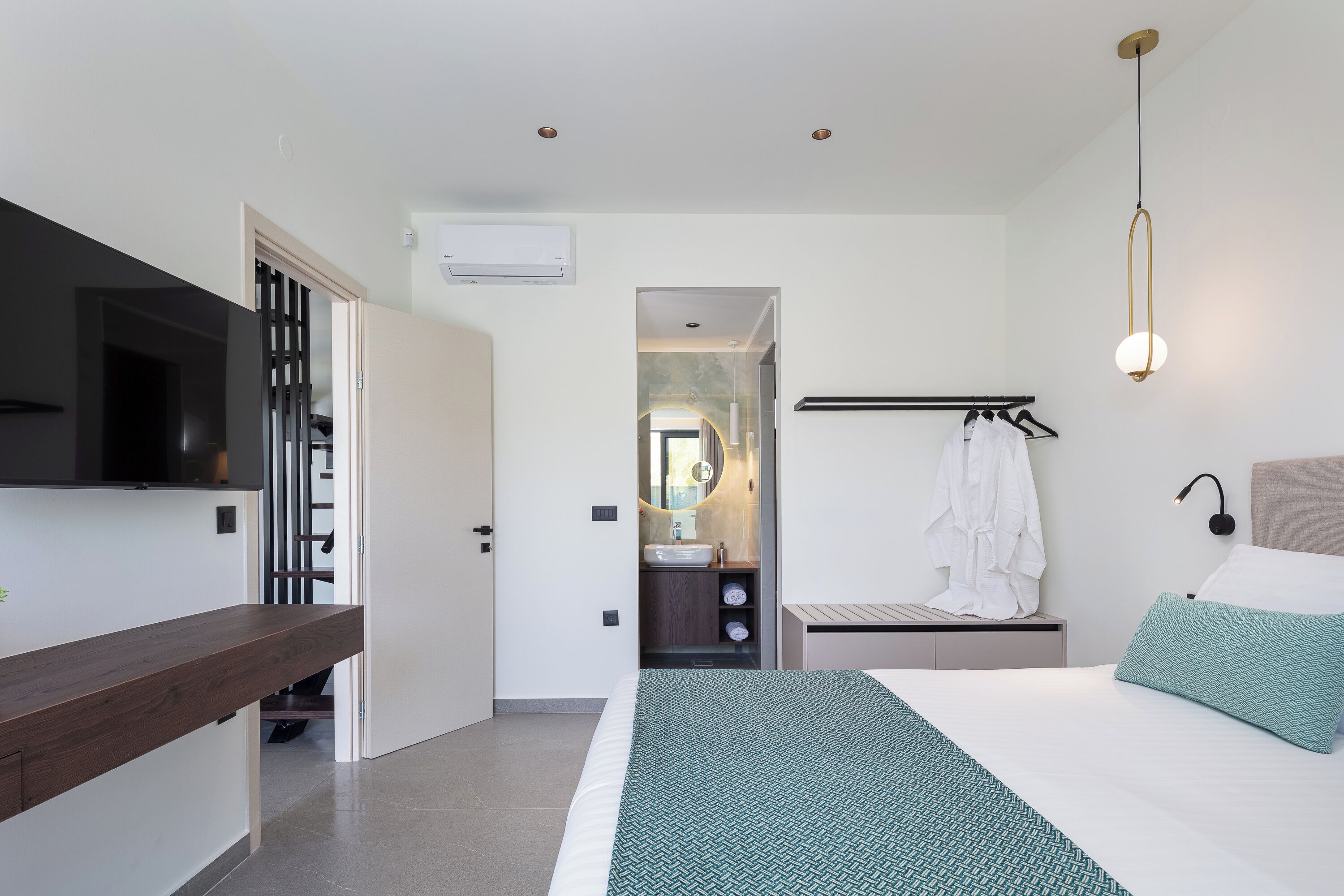 Una habitación de hotel moderna con una cama grande, un televisor montado en la pared, una mesita de noche y una lámpara colgante.