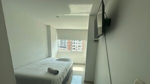 A small, clean room with a bed, a TV mounted on the wall, and a window with a city view. - FURNISHED APARTMENT IN SOTOMAYOR CABECERA (Bucaramanga)