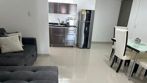 A modern living room with a grey sofa and a dining area with white chairs and a glass table. - FURNISHED APARTMENT IN SOTOMAYOR CABECERA (Bucaramanga)