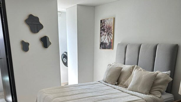 A modern bedroom with a large bed, a headboard, and a wall-mounted artwork. - FURNISHED APARTMENT IN SOTOMAYOR CABECERA (Bucaramanga)