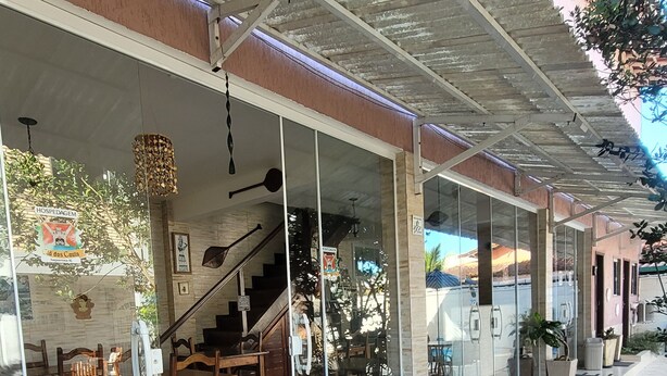 A covered outdoor area with a tiled floor, glass doors leading to an interior space with wooden furniture, and a staircase. - HOSPEDAGEM CLÃ DOS COUTO (Saquarema)