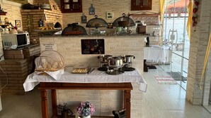 A kitchen with a brick wall, a white table with a basket of bread, and a window with yellow curtains. - HOSPEDAGEM CLÃ DOS COUTO (Saquarema)