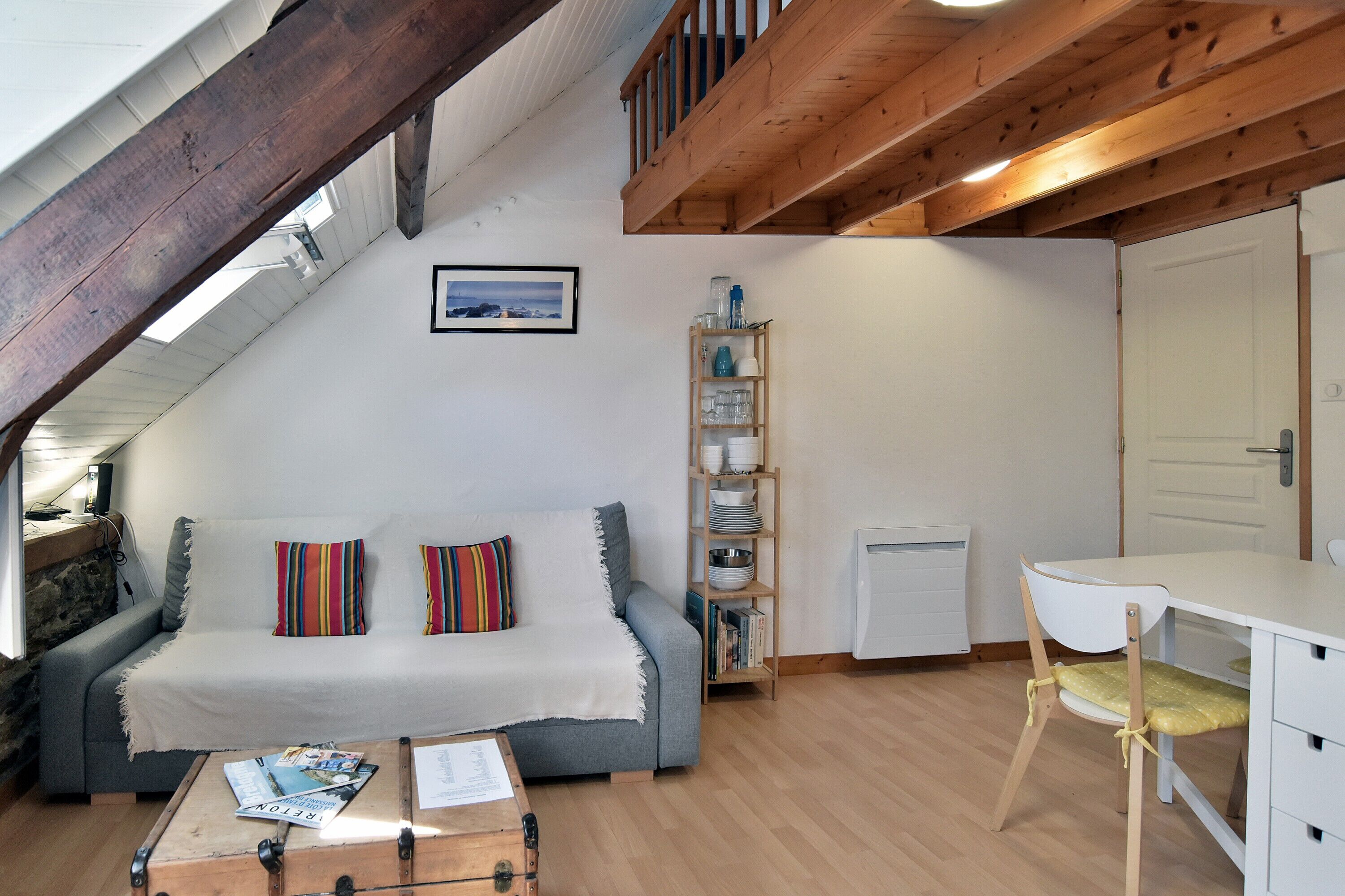 Et hyggeligt loftrum med hems, sofa, spisebord og bogreol.