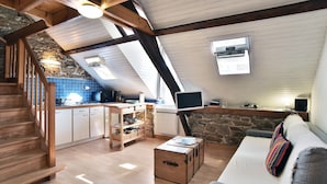 Un espace de vie de style loft avec un escalier en bois, un coin cuisine et un coin salon confortable avec un canapé et une petite table.