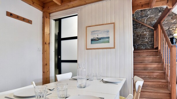 Une table à manger dressée avec des assiettes, des verres et des couverts, un tableau encadré accroché au mur et un escalier en bois menant à un mur en pierre.