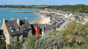 Une ville côtière avec une plage, des voitures garées et des bâtiments aux façades en pierre.