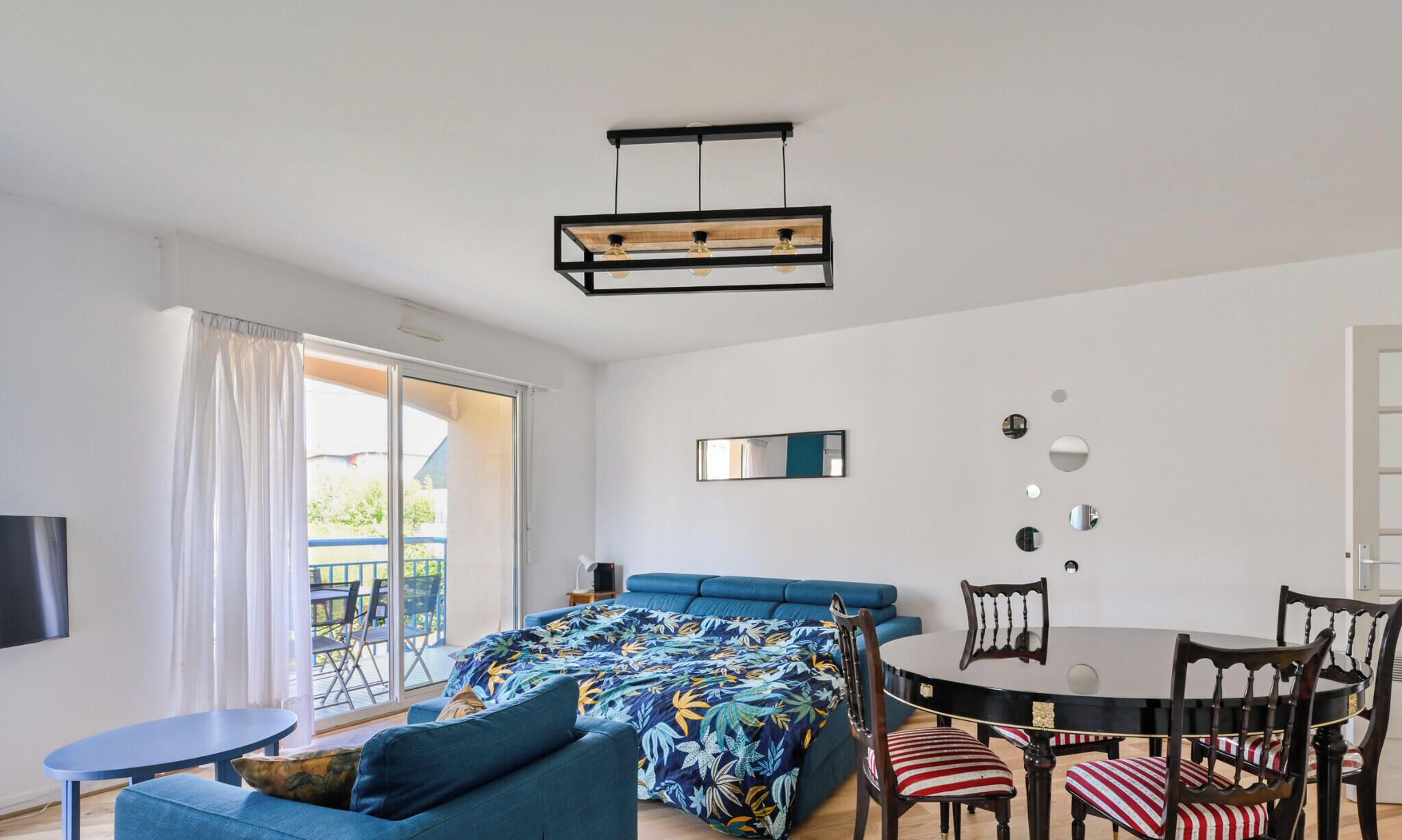 Une pièce comprenant un lit, un canapé, une table à manger avec des chaises, un luminaire au plafond et une porte-fenêtre coulissante donnant sur un espace extérieur.
