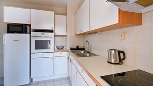A compact kitchen with white cabinets, a microwave, an oven, a sink, and a kettle.