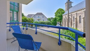 A balcony with blue chairs, a view of a church, and a building with a tower.