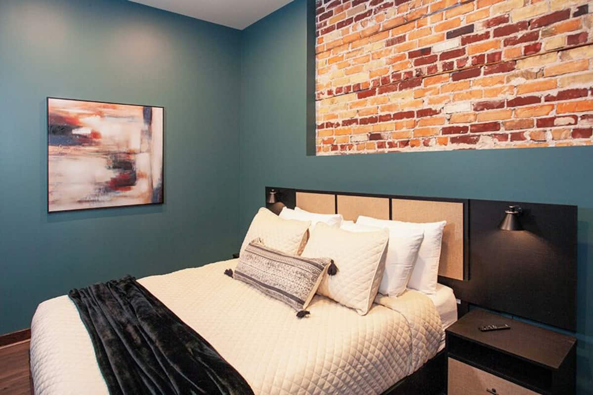 A bedroom with a bed, a headboard, a nightstand, a lamp, and a brick wall.