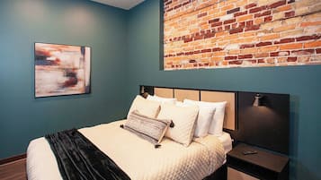 Une chambre à coucher avec un lit, une tête de lit, une table de chevet, une lampe et un mur en briques.