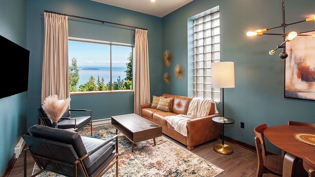 A living room with a view of the sea, a brown leather sofa, a coffee table, and a dining table. - The Intrepid (Duluth)