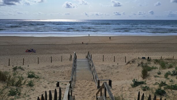 Een houten looppad dat naar een zandstrand leidt, met uitzicht op de oceaan.