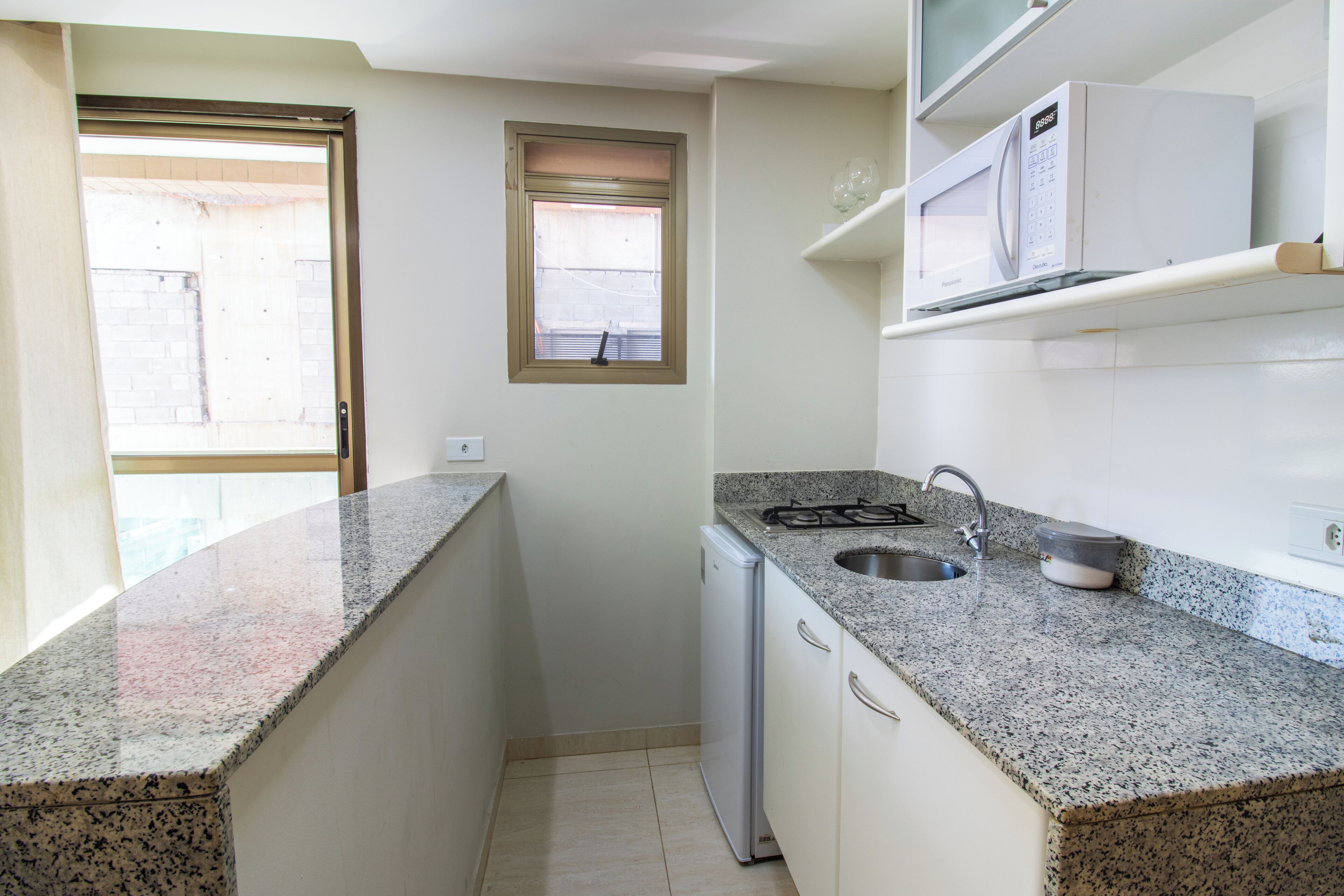 A compact kitchen with granite countertops, a built-in dishwasher, and a microwave on a shelf.