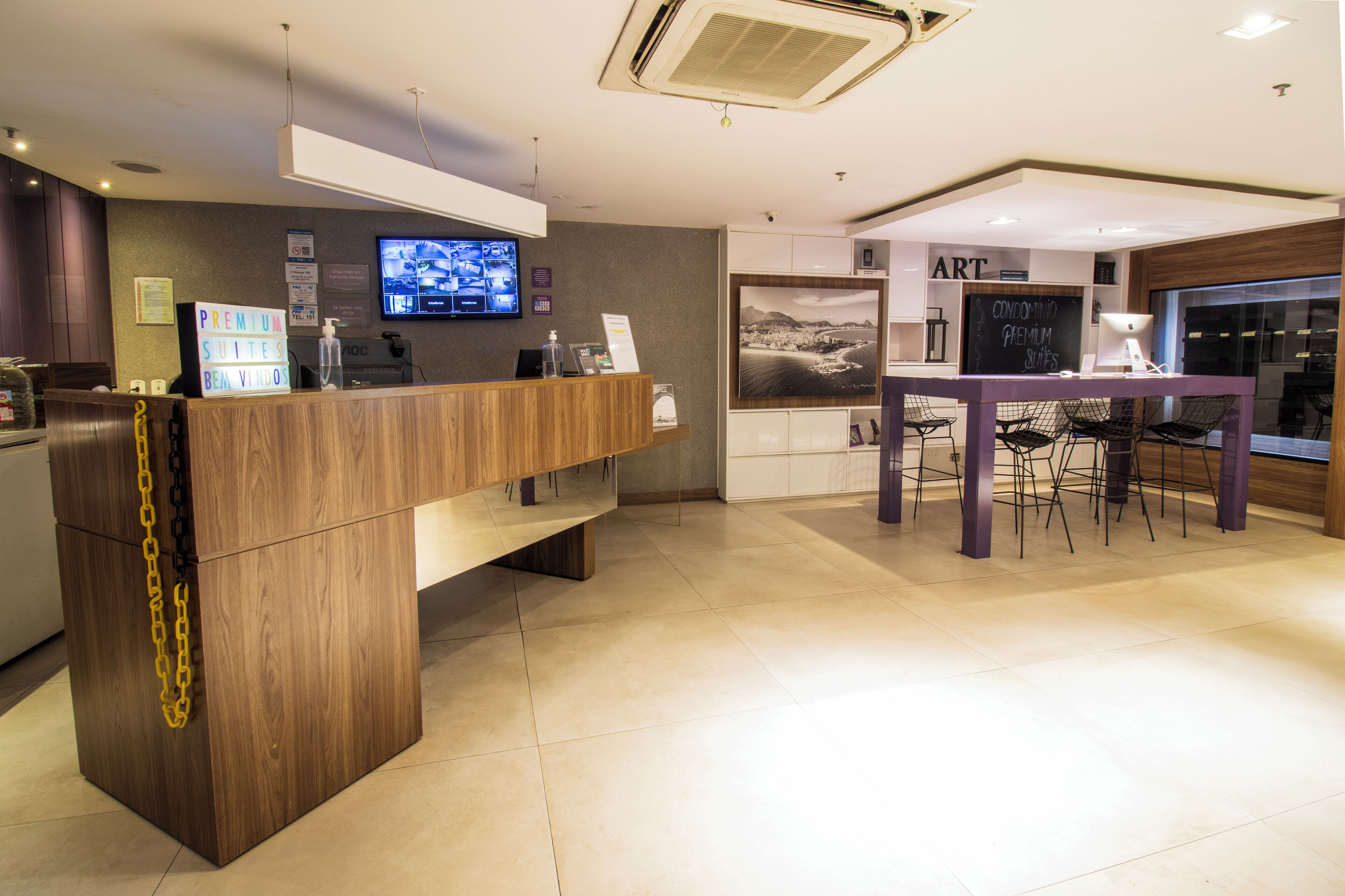 A hotel reception area with a wooden reception desk, a television mounted on the wall, and a chalkboard with text.