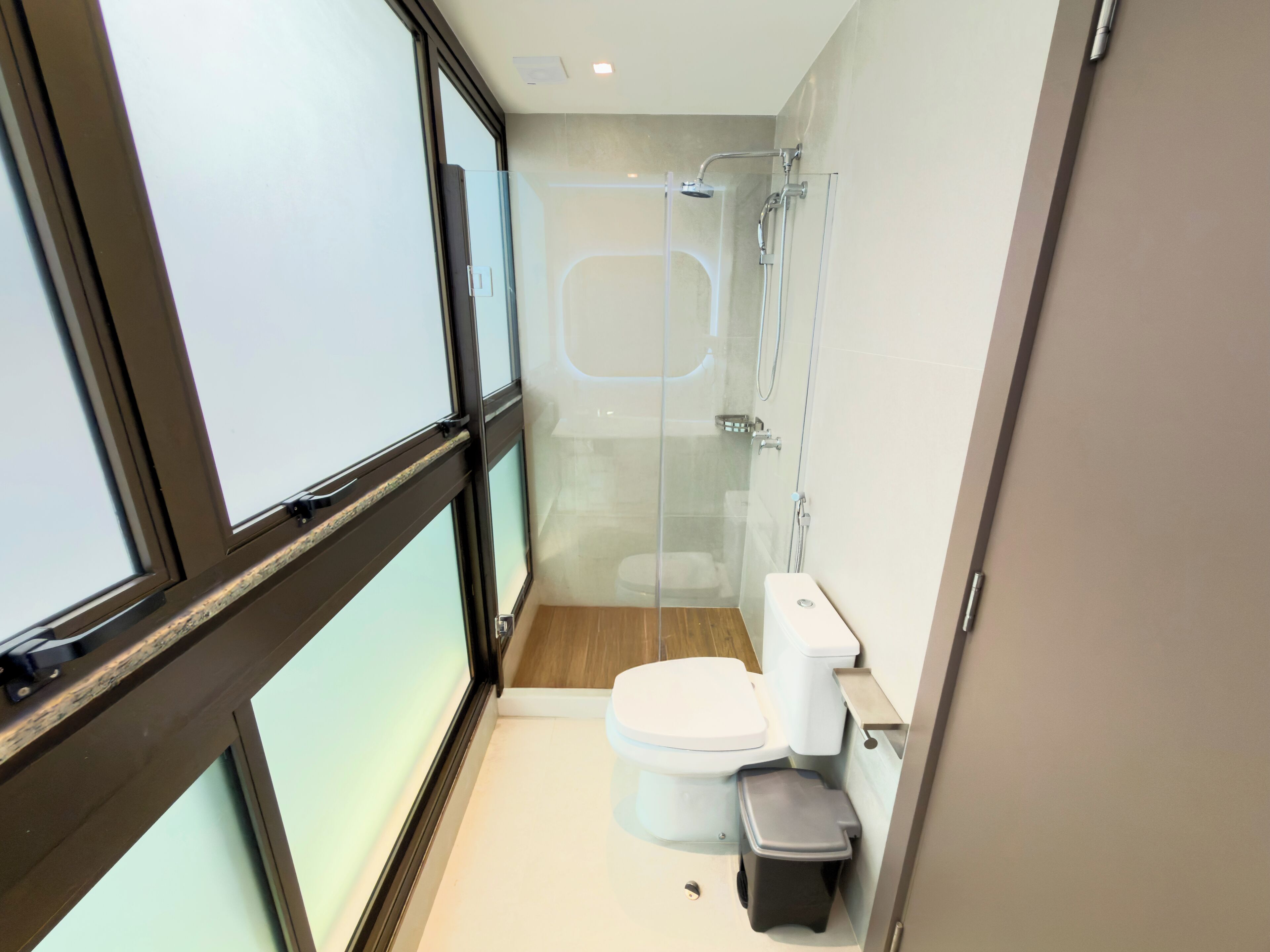 A modern bathroom with a glass-enclosed shower, a toilet, and a trash bin.