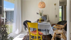 Ruokailutila, jossa on ruutukuviollinen pöytäliina, keltainen tuoli ja punottu riippuvalaisin.