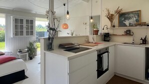 Moderni keittiö, jossa on valkoiset kaapit, sisäänrakennettu uuni ja suuri keittiösaareke, jossa on pesuallas. Keittiössä on myös ruokailutila, jossa on pöytä ja tuolit, ja sieltä on näkymä ulos.