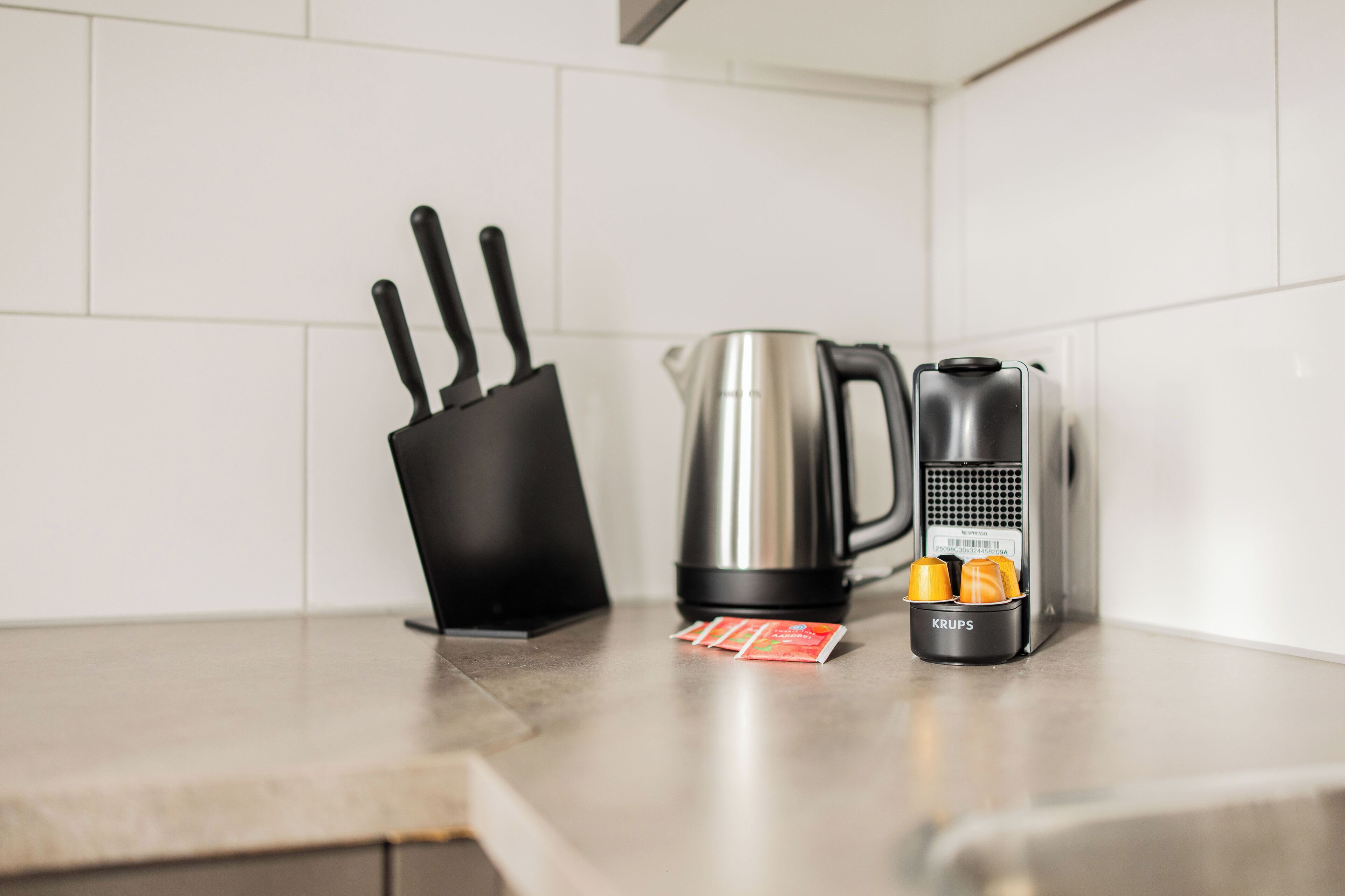 Un plan de travail de cuisine avec une machine à café, une bouilloire et un moulin à café Krups.