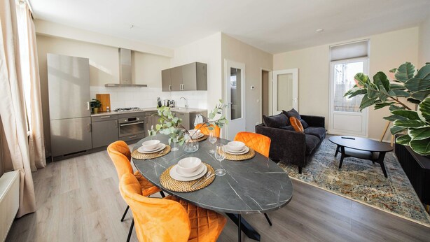 A modern living room with a dining area, featuring a dark marble table, orange chairs, and a black sofa. - Zwart Janstraat  (Rotterdam)