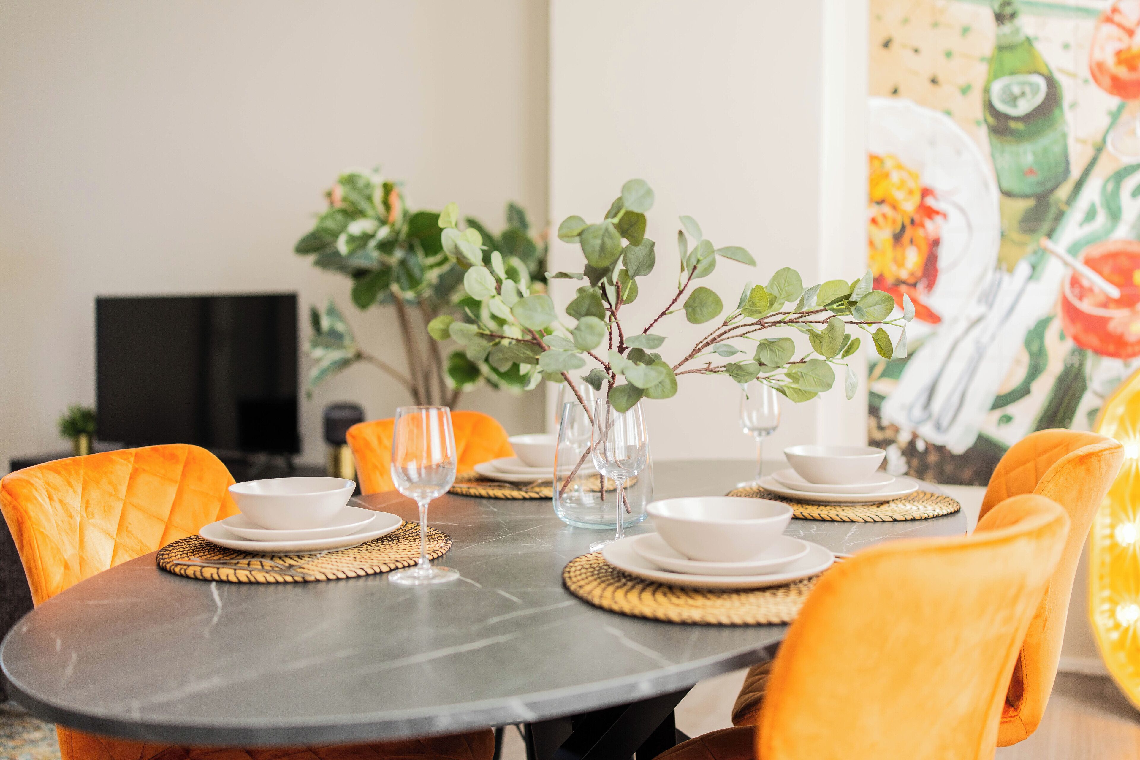Une table à manger dressée avec de l’argenterie blanche, des assiettes, des bols et des verres, entourée de chaises orange.