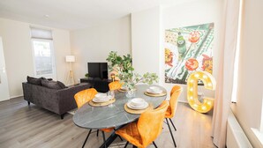 A modern living room with a dining area, a grey sofa, orange chairs, and a large decorative number '6' sign. - Zwart Janstraat  (Rotterdam)