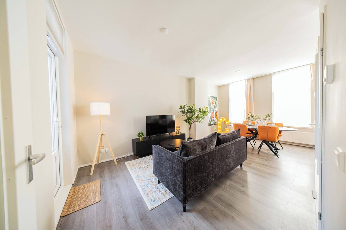 Ett modernt vardagsrum med en soffa, en tv och en matplats med orangefärgade stolar.