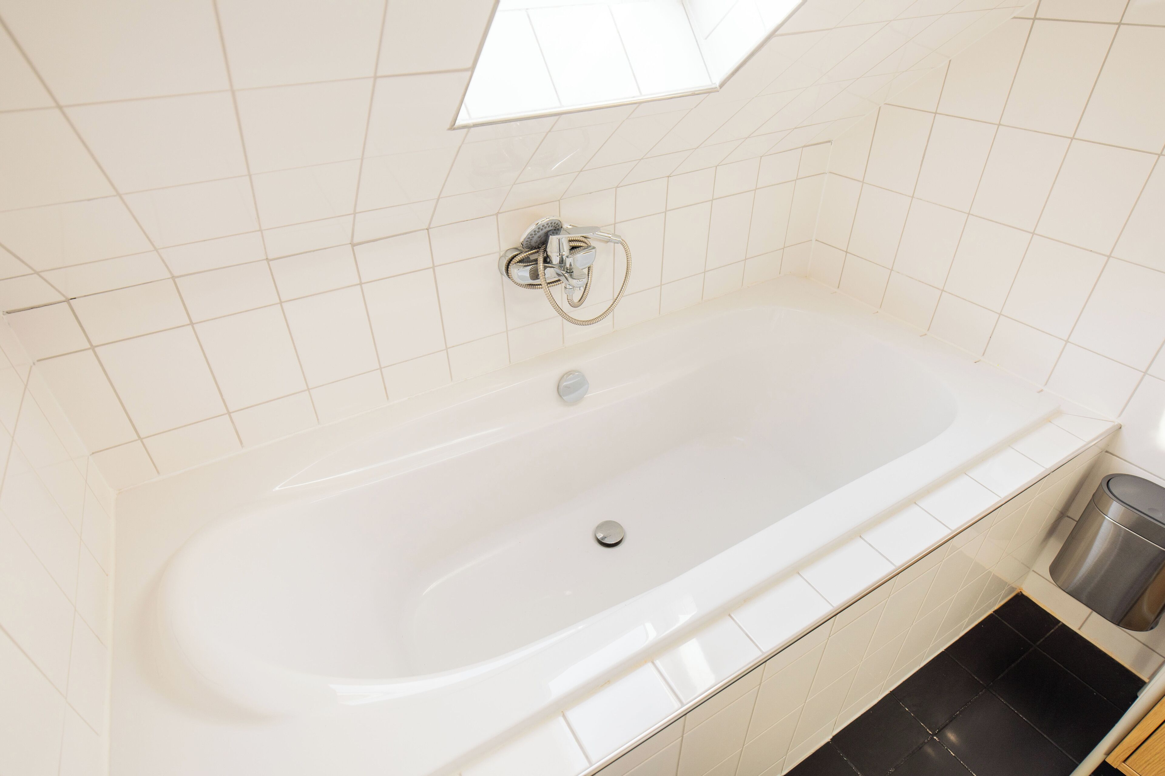 Een moderne badkamer met een groot, wit bad, douchekop en een prullenbak.