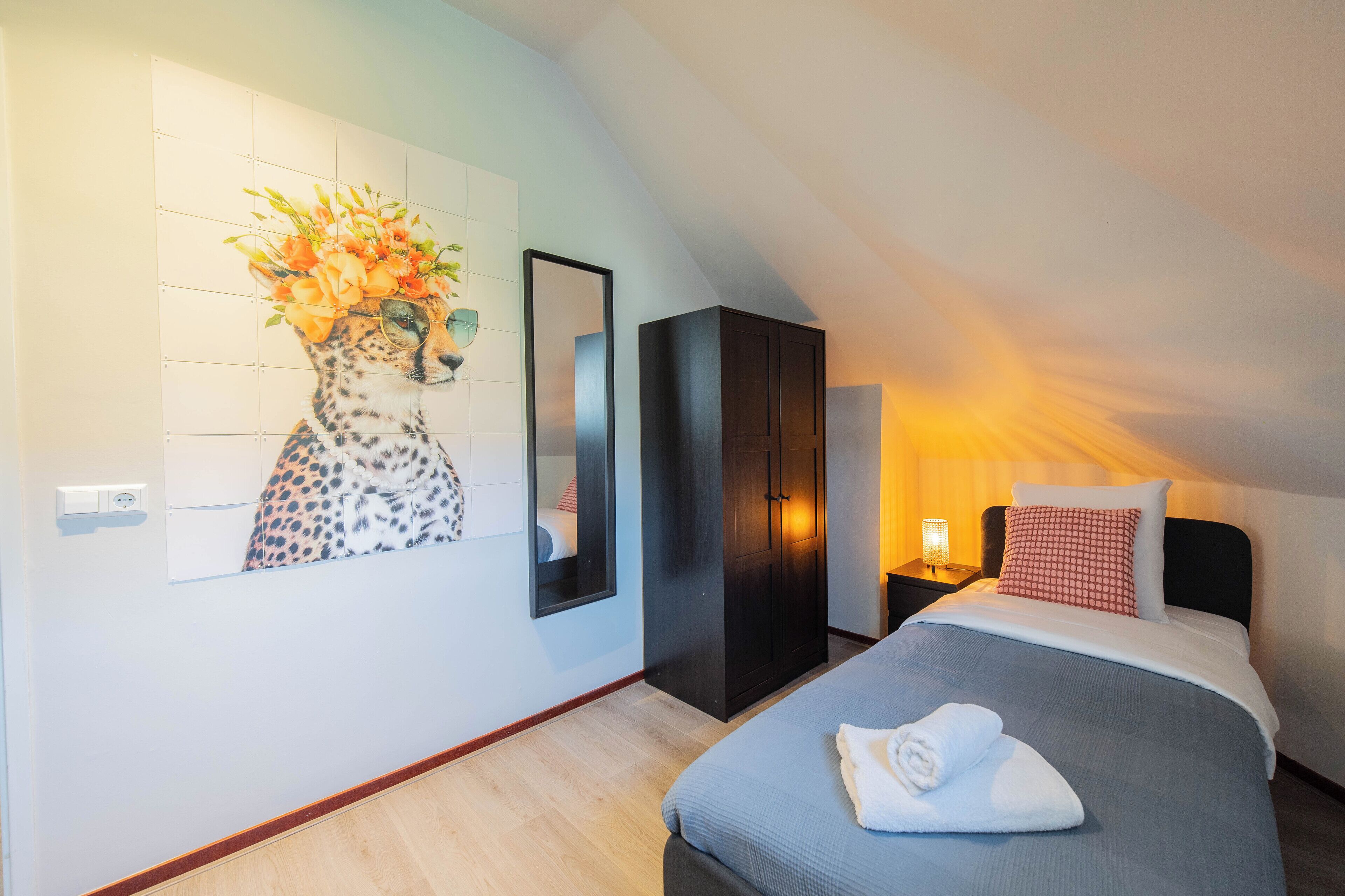 A bedroom with a bed, a wardrobe, a mirror, and a wall art of a cheetah with flowers.