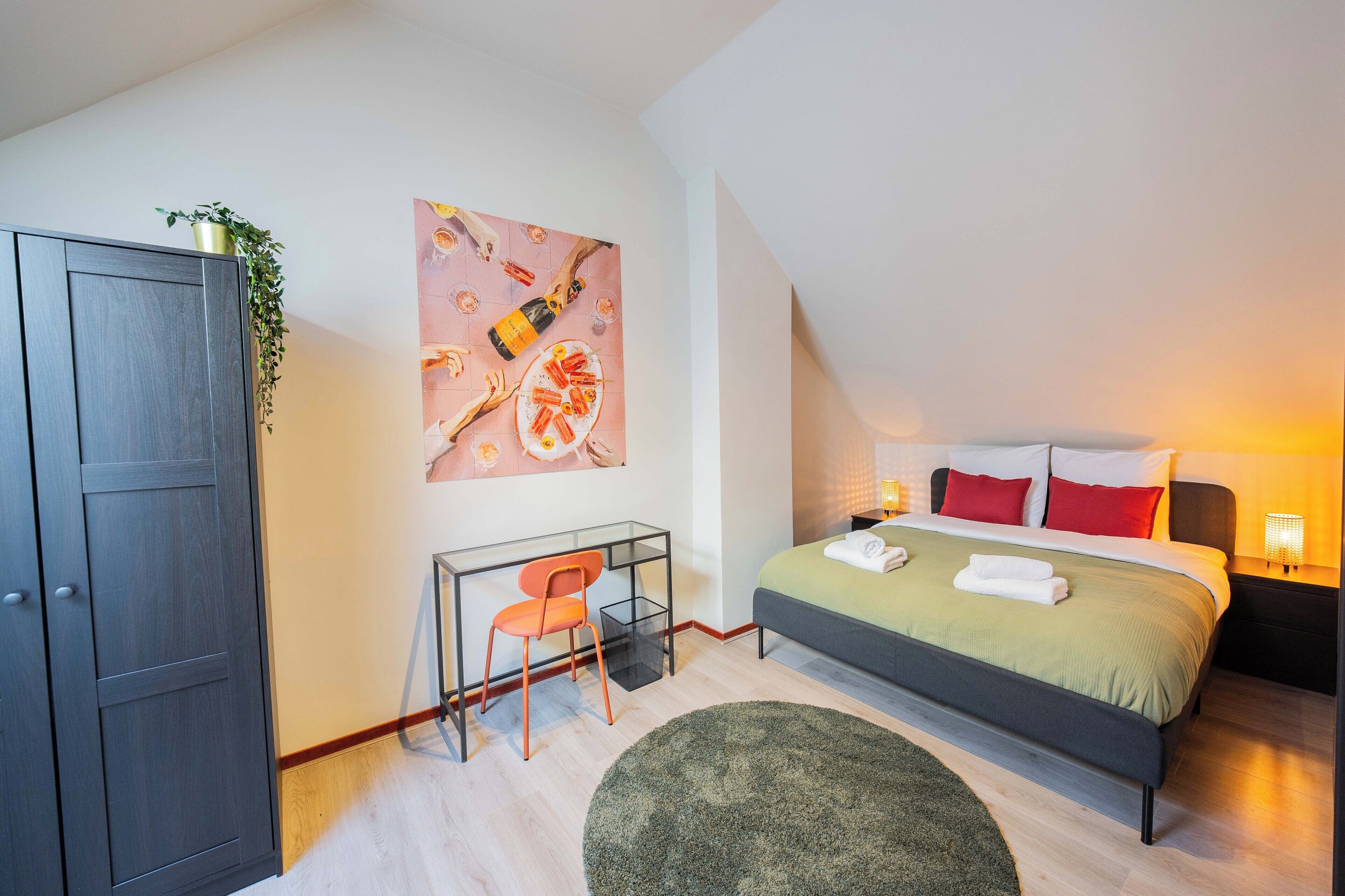 A modern bedroom with a bed, desk, and chair, a large painting on the wall, and a plant on the desk.