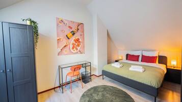 A modern bedroom with a bed, desk, and chair, a large painting on the wall, and a plant on the desk.