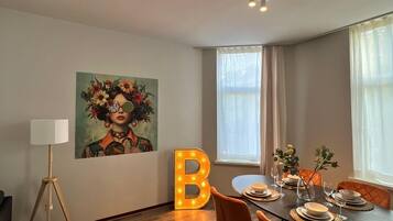 Un comedor con una mesa dispuesta para cuatro, una gran 'B' iluminada en la pared y un cuadro sobre la mesa.