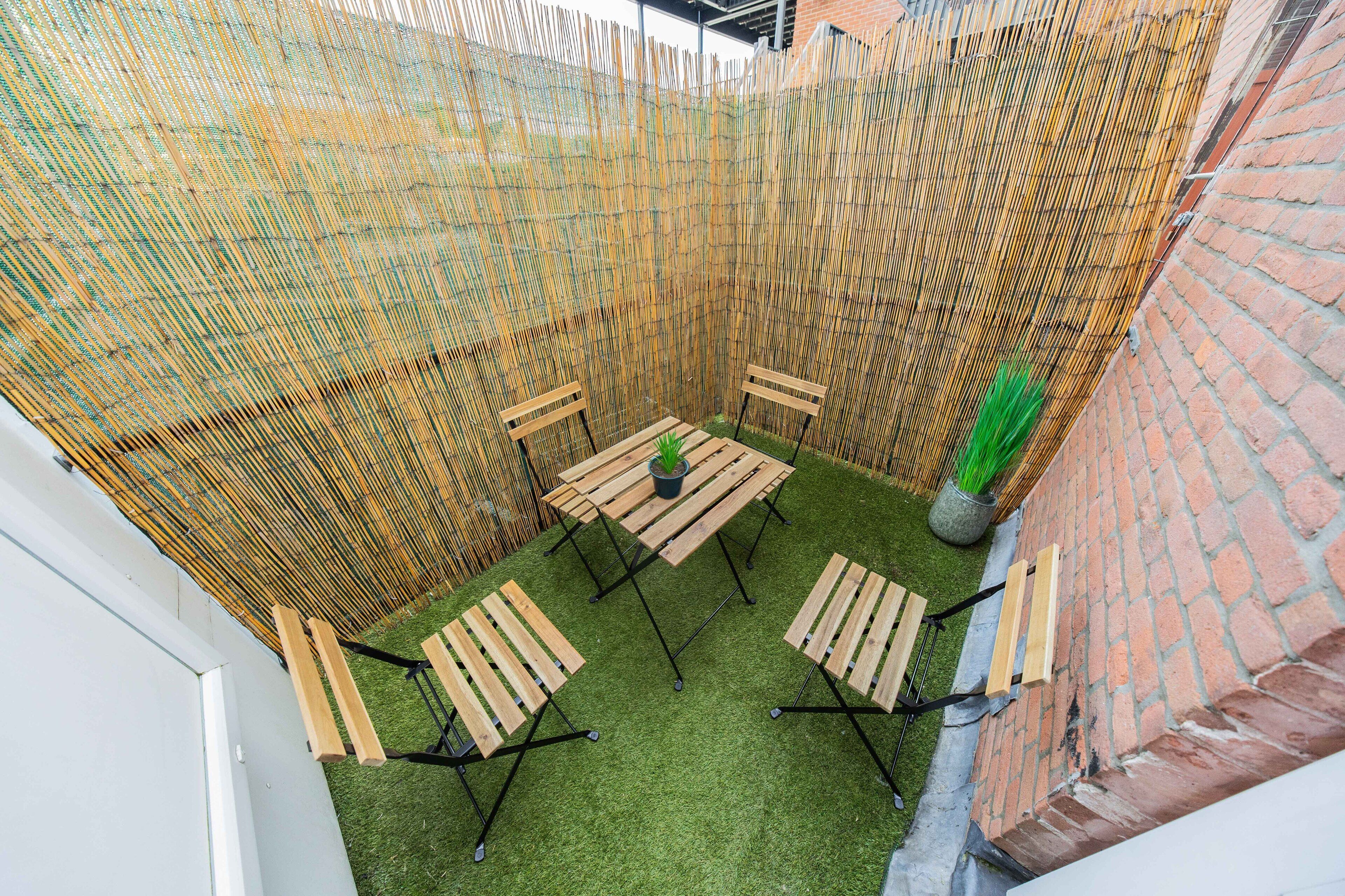 Un'area patio con una recinzione in bambù, un muro in mattoni e un tavolino con sedie.