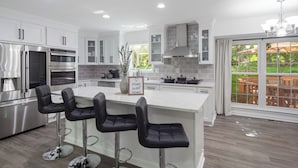 A modern kitchen with white cabinetry, stainless steel appliances, and a central island with bar stools. - Modern and Spacious 4-bedroom house close to DC and National Harbor (Fort Washington)