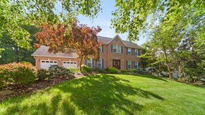 A two-story brick house with a well-maintained lawn, a garage, and mature trees with autumn foliage. - Modern and Spacious 4-bedroom house close to DC and National Harbor (Fort Washington)