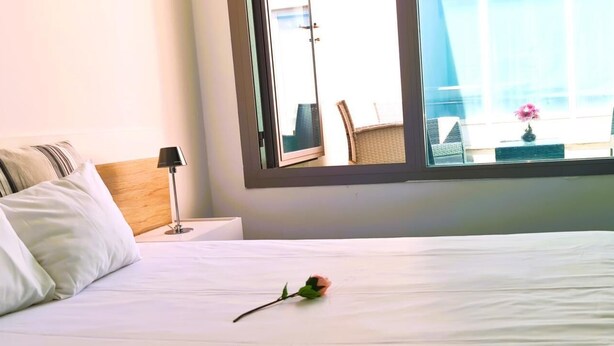 A hotel room with a bed, a nightstand, a lamp, and a window with a view of outdoor seating.