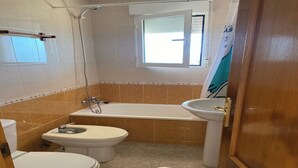 Ett badrum med två toaletter, ett badkar och ett handfat.