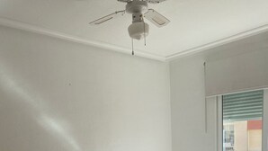 Ett sovrum med en säng, ett nattduksbord, en lampa, en takfläkt och ett fönster med persienner.