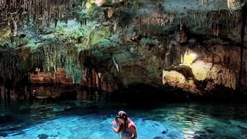 Une personne se trouve dans une grotte où l’eau est claire et où il y a des stalactites.
