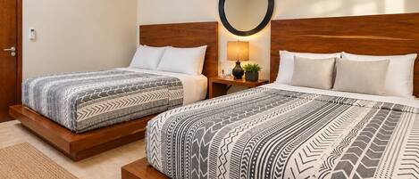 A hotel room with two beds, a round mirror, a nightstand with a lamp, and a small potted plant.