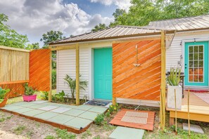 Una pequeña casa con puerta verde, cerca de madera y jardín con plantas en macetas.