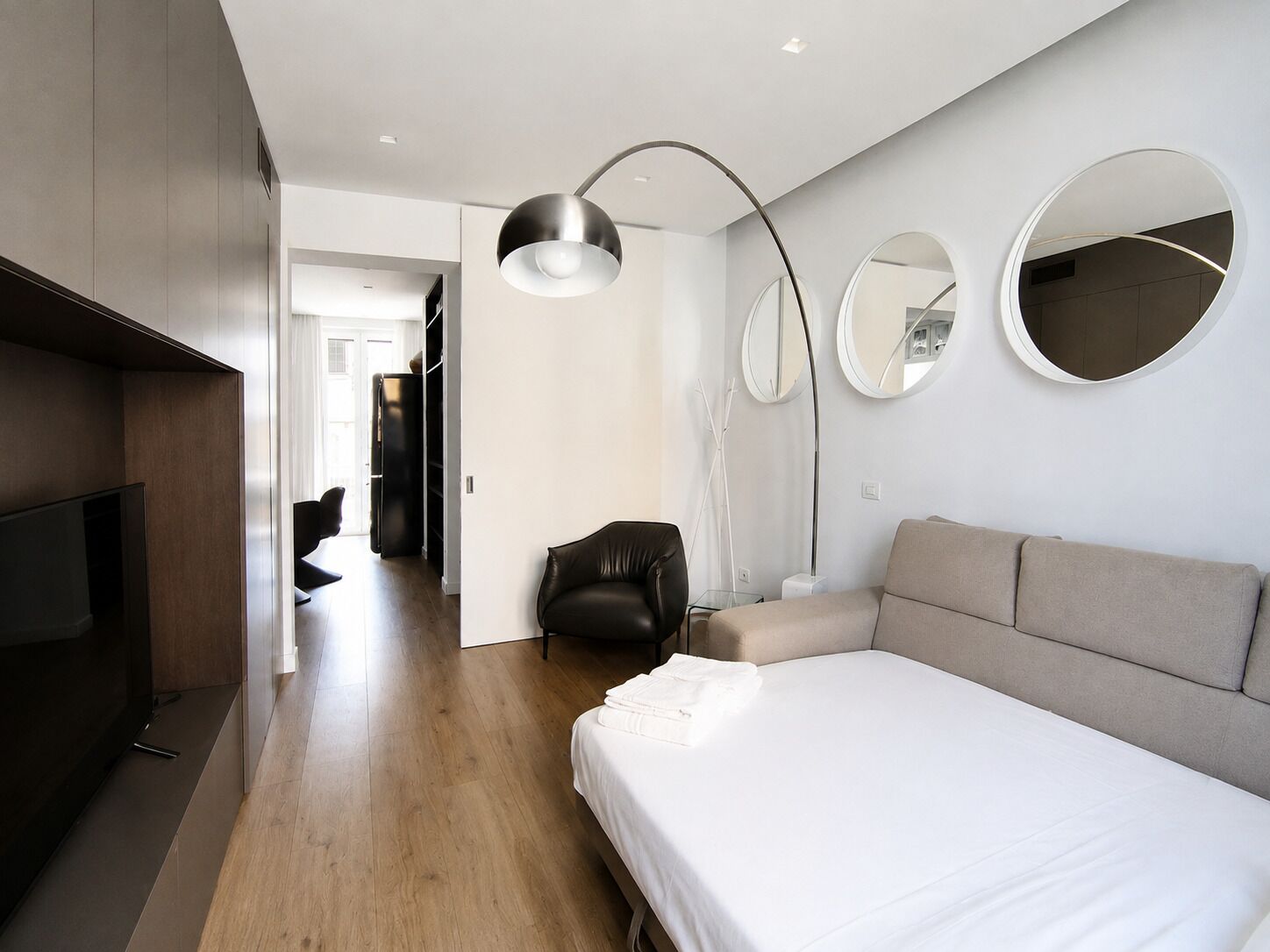 A modern hotel room with a large bed, a flat-screen TV, a desk, and a chair. There are two round mirrors on the wall.
