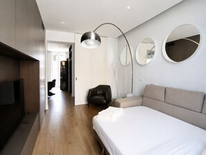 A modern hotel room with a large bed, a flat-screen TV, a desk, and a chair. There are two round mirrors on the wall.