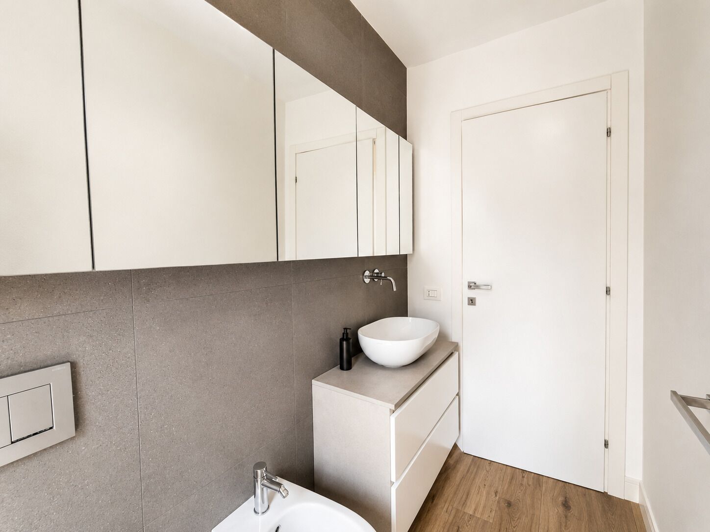 Une salle de bain moderne avec un lavabo blanc, un miroir et une porte.