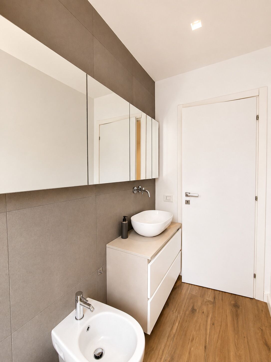 Un baño moderno con un lavamanos blanco, un espejo y una puerta.