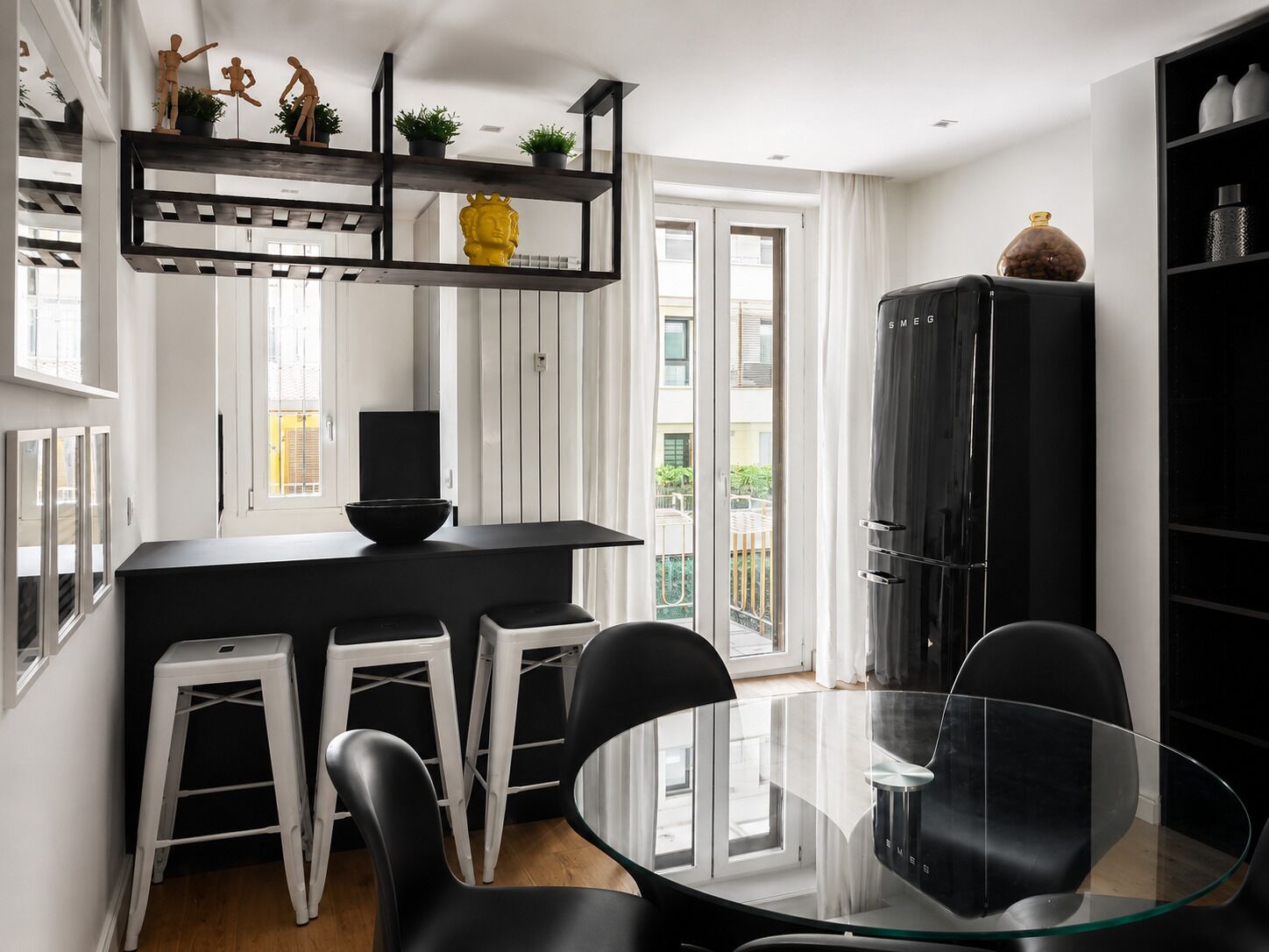 Una cocina moderna con encimera negra, taburetes blancos y una mesa de comedor de vidrio.