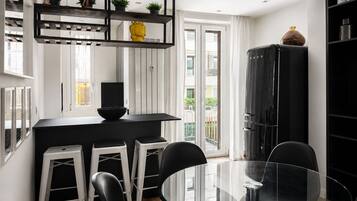 Una cocina moderna con encimera negra, taburetes blancos y una mesa de comedor de vidrio.