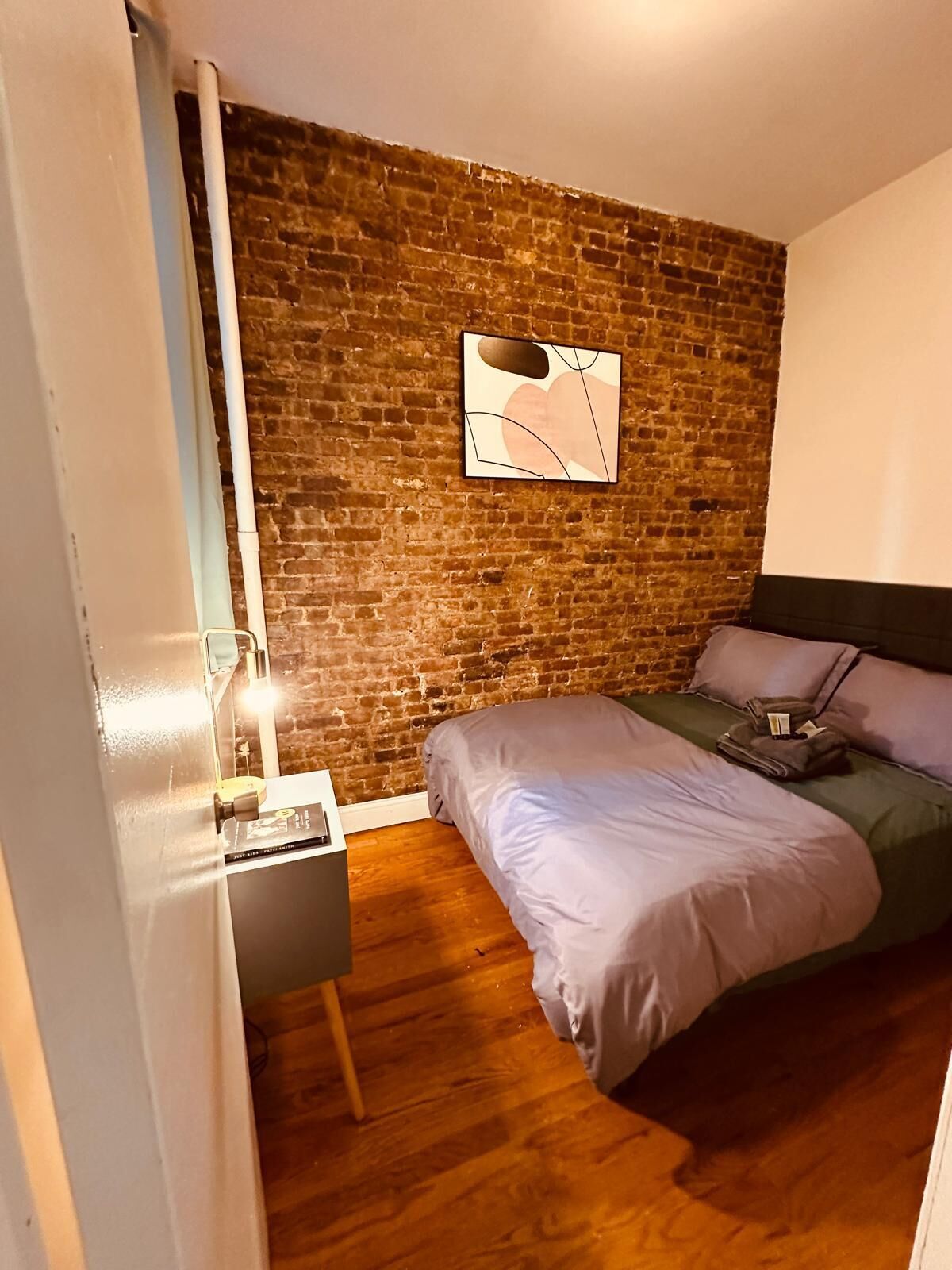 Ein Schlafzimmer mit Backsteinwand, einem Bett, einem Nachttisch und einem Wandbild.