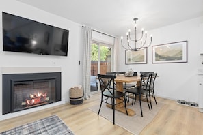 A modern living room with a fireplace, a dining table with chairs, a TV mounted on the wall, and framed artwork on the wall. - Private Hot Tub + Sauna · Lakeside · Dog-Friendly · Trails (Frisco)